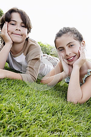 Boy And Girl Resting Chin In Hands While Lying On Grass