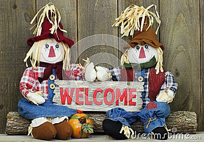 Boy and girl scarecrows sitting on log holding red wood welcome sign