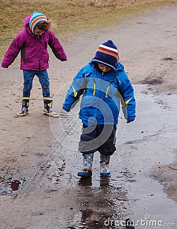 Boy and girl splashing in a muddy puddle
