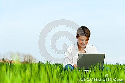 Boy in green field with laptop.