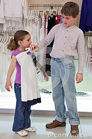 The boy helps sister to choose clothes in shop