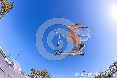 Boy jumps with his scooter at a skate park