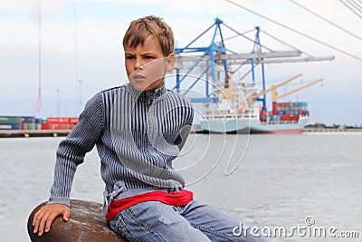 Boy sits on stone at background of ship