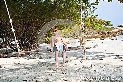 Boy sitting on a swing at the beach