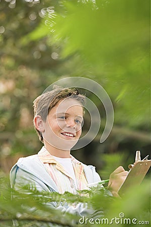 Boy Writing On Clipboard In Forest