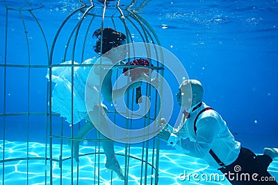Bride and groom and a birdcage underwater pool water dive