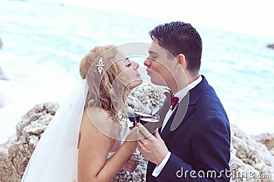 Bride and groom drinking red wine at the ocean