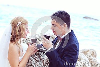 Bride and groom drinking red wine at the ocean