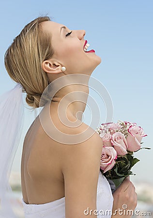 Bride With Her Head Back Holding Flower Bouquet Against Sky