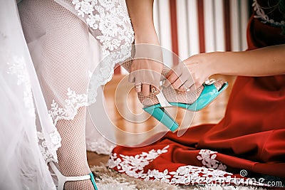 Bridesmaid helps to bride to put on wedding shoes.