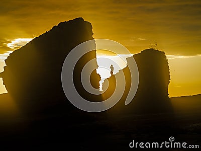 Bright yellow sun on the sea stacks with silhouette of a person standing on the top of a rock