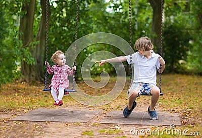 Brother and baby sister on swing on playground