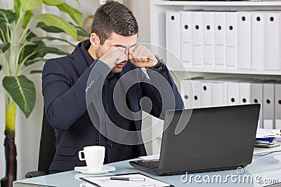 Business man rubs his eyes from the bad news at the office