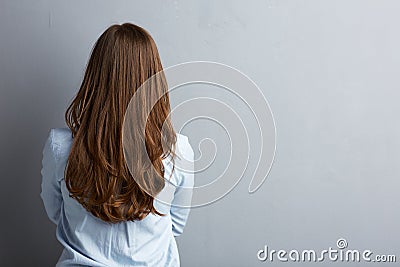 Business woman standing back against gray wall.