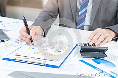 Businessman analyzing report on chart with laptop and calculator