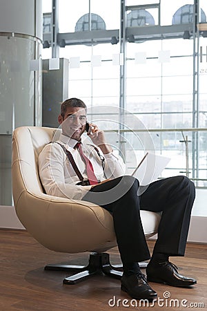 Businessman in arm chair working on laptop on the phone