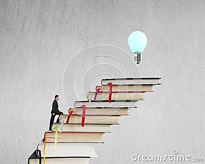 Businessman climbing on stack of books to reach top with bulb