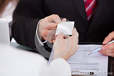 Businessman giving visiting card to colleague at desk