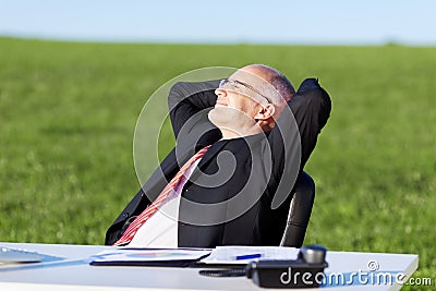 Businessman With Hands Behind Head At Desk On Field