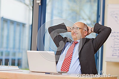 Businessman With Hands Behind Head Sitting At Desk