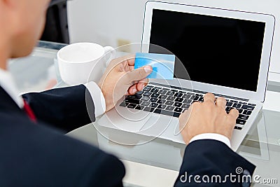 Businessman holding credit card by a laptop keyboard