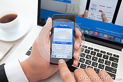 Businessman holding iPhone with app PayPal on the screen on a ba