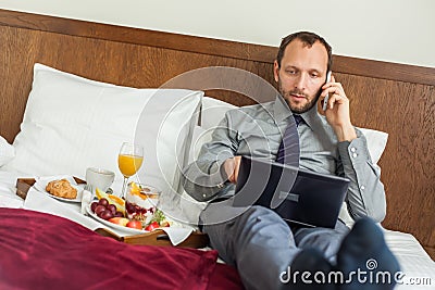 Businessman with laptop during breakfast. He is lying on bed.