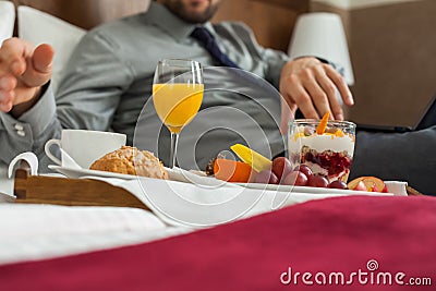 Businessman with laptop during breakfast. He is lying on bed.