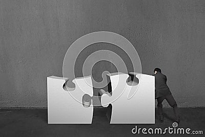 Businessman push two heavy puzzles together in concrete wall bac