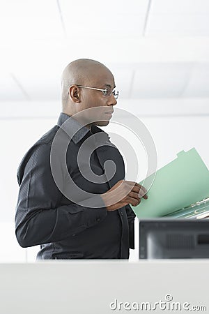 Businessman Reviewing File At Computer Desk