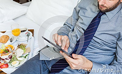 Businessman with tablet computer during breakfast. He is lying o