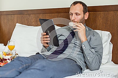 Businessman with tablet computer during breakfast. He is lying o