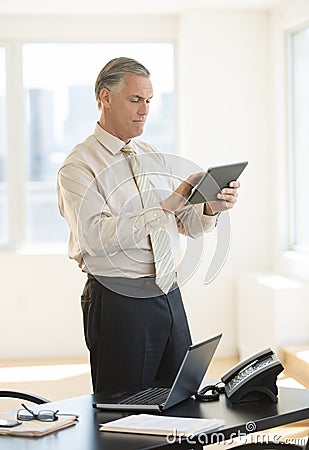 Businessman Using Digital Tablet While Standing By Desk