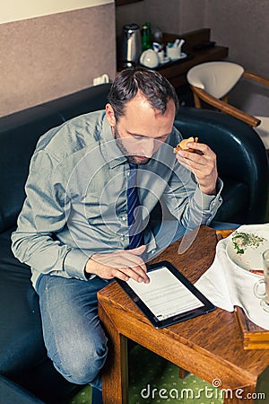 Businessman working on tablet pc during breakfast at home/hotel.