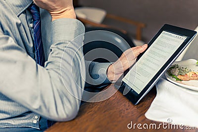 Businessman working on tablet pc during breakfast at home/hotel.