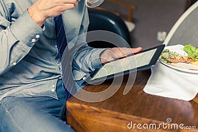 Businessman working on tablet pc during breakfast at home/hotel.