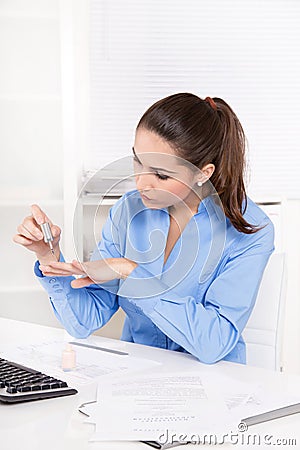 Businesswoman in a blue blouse is making her nails at desk