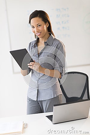 Businesswoman With Digital Tablet Standing By Desk In Office