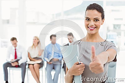Businesswoman gesturing thumbs up against people waiting for interview