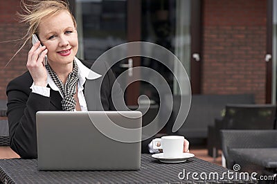 Businesswoman on phone outdoors with laptop and cup of coffee