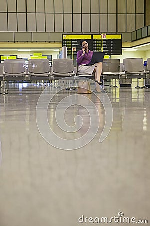 Businesswoman Using Cellphone And Laptop In Airport Lobby