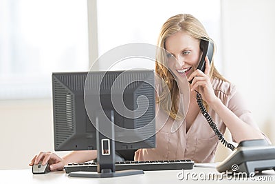 Businesswoman Using Computer While Conversing On Landline Phone