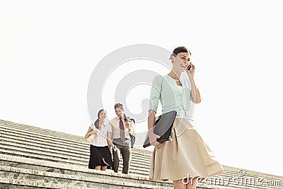 Businesswoman Using Mobile Phone On Steps With Colleagues In Bac