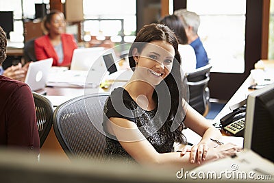 Businesswoman Working At Desk With Meeting In Background