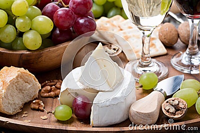 Camembert, fresh baguette, grapes and wine on wooden tray