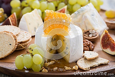 Camembert with honey and fruit close-up on a wooden tray