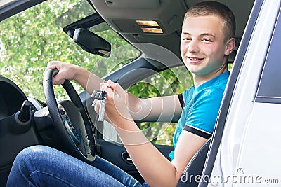 Car driver. Caucasian teen boy showing car key in the new car.