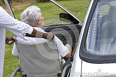 Caregiver helping a disabled senior lady to get inside of her car