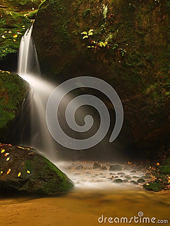 Cascade on small mountain stream, water is running over mossy sandstone boulders and bubbles create on level milky water.