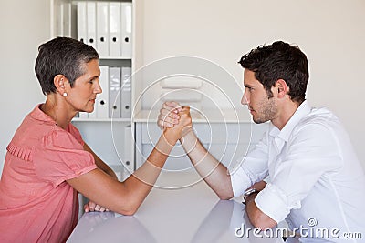 Casual business team arm wrestling at desk